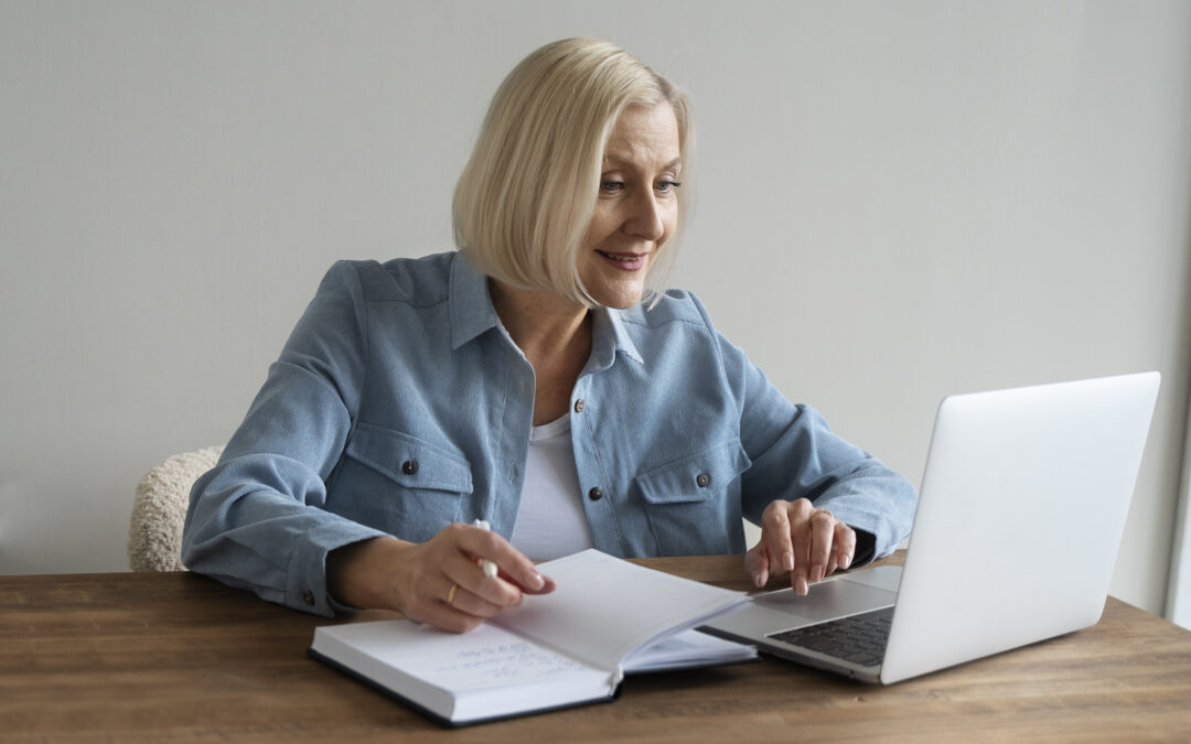 older woman using a laptop and a notebook to write