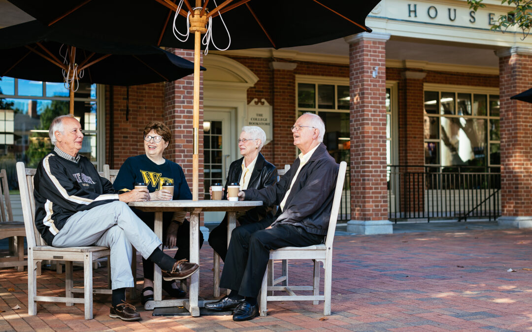 Four seniors dressed in Wake Forest University gear enjoy coffee on campus.