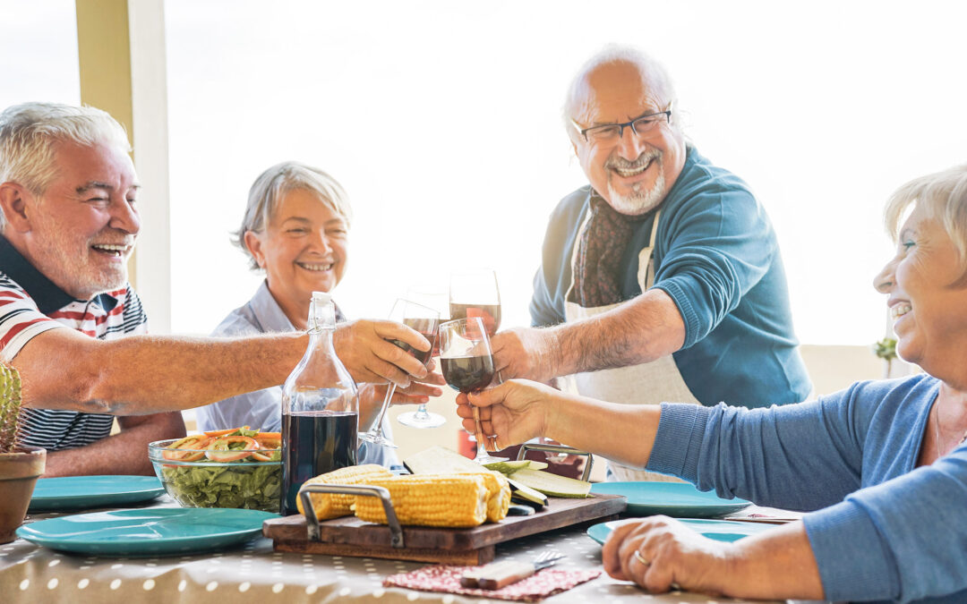 Happy senior friends toasting with red wine at barbecue dinner in terrace